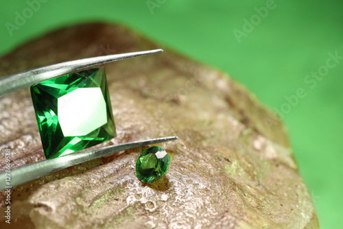 Tweezers with beautiful green gemstones on stone, closeup. Space for text