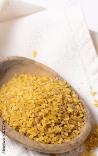 Raw dry uncooked yellow bulgur grain in a wooden bowl on white table cloesup. Ancient food photo