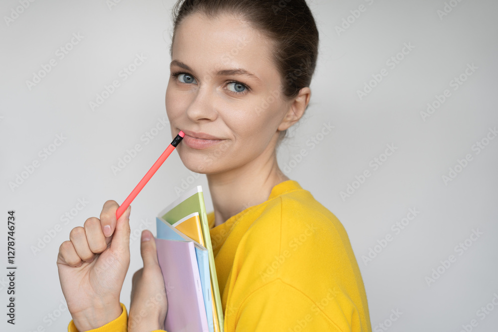 a beautiful young female student with a pencil in her hand rests on her cheek, smiles thoughtfully and looks at the camera, gray background a beautiful young female student with a pencil in her hand rests on her cheek, smiles thoughtfully and looks at the camera, gray background