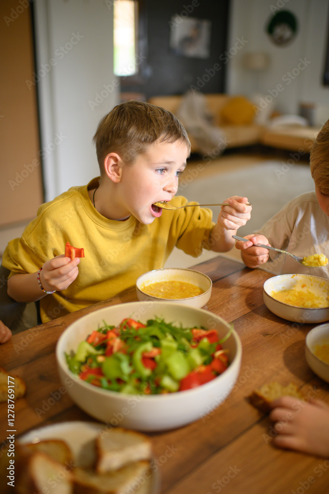 A young boy enjoys a healthy meal with his family, eating soup and salad with great appetite. The scene reflects wholesome nutrition, warmth, and togetherness at the dining table. A young boy enjoys a healthy meal with his family, eating soup and salad with great appetite. The scene reflects wholesome nutrition, warmth, and togetherness at the dining table.