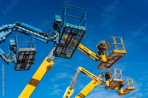 Colorful industrial telescopic boom lift jibs and platforms raised high in the air before very busy construction building season starts. Heavy industrial lifts on blue sky background