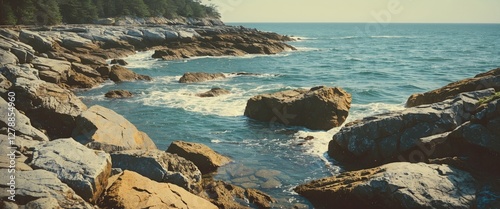 Rocky shoreline with waves crashing against boulders and calm ocean water under a clear sky in coastal landscape setting. photo