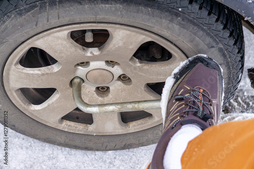 man unscrewing a car wheel with a wrench. seized bolts in an aluminum rim. loosening bolts in a wheel with a wrench and foot. wheel replacement photo