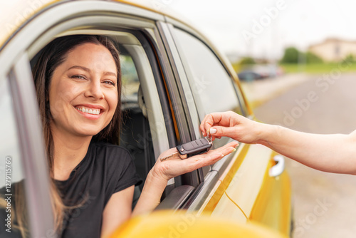 Obraz na płótnie A smiling woman sitting in a yellow car receives a set of keys from another person, symbolizing a car purchase, rental, or ownership transfer. w salonie