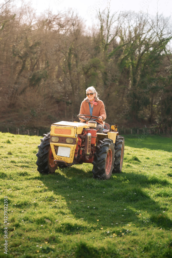 Obraz premium Senior woman farmer driving a tractor in a green field, celebrating her contribution to agriculture on international workers' day