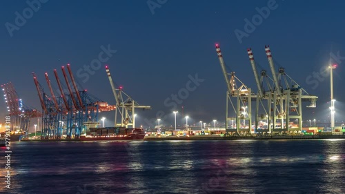 Night timelapse of Hamburg cargo port, showcasing container terminals, cranes and cargo ships on the Elbe River. Boats and vessels pass by, creating a dynamic maritime panorama. Germany