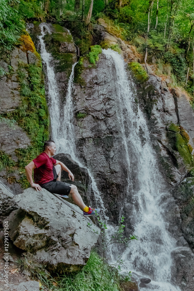 Obraz premium A man is peacefully sitting on a large rock near a beautiful waterfall