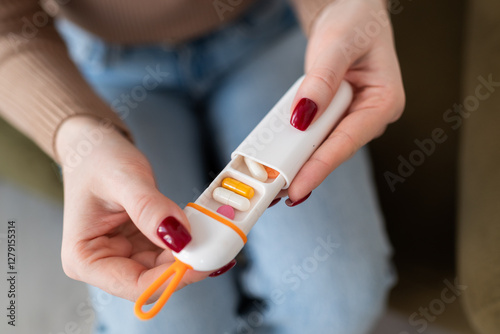 Woman holding a portable pill case with various capsules and tablets. Compact travel medicine organizer for daily health and medication management.