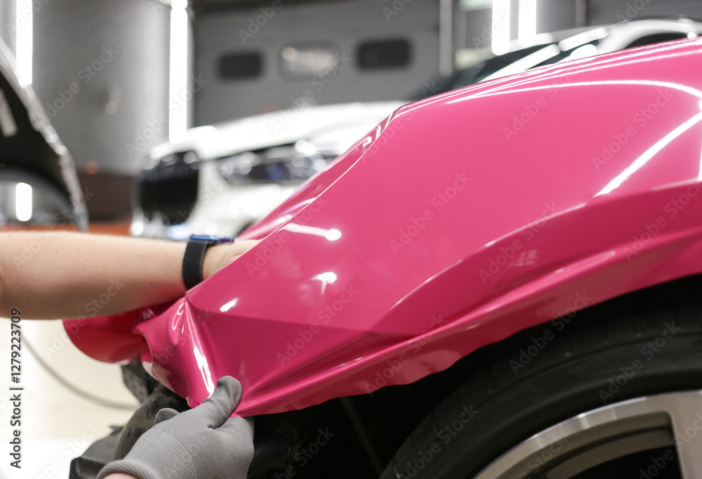 A specialist in wrapping a car with pink-colored vinyl film in the process of work. Car wrapping specialists cover the car with vinyl sheet or film. Car wrapping close-up. Selective focus. A specialist in wrapping a car with pink-colored vinyl film in the process of work. Car wrapping specialists cover the car with vinyl sheet or film. Car wrapping close-up. Selective focus.