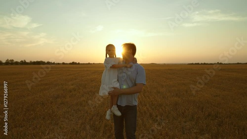 Father holding kid in arms in field at sunset. Happy cheery parent child kid strolling moving going across huge yellow meadow. Girl sits in man arms pointing with finger. Love fatherhood parenthood