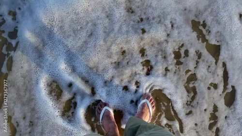 Zenithal view of the sea reaching the sand, conceptual summer video with negative space. White flip flops are seen.