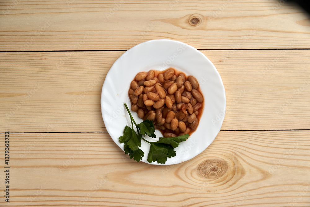 Fototapeta premium A plate of beans and parsley sits on a wooden table. The beans are spread out and appear to be cooked. The parsley is placed on the edge of the plate, adding a pop of color and freshness to the dish