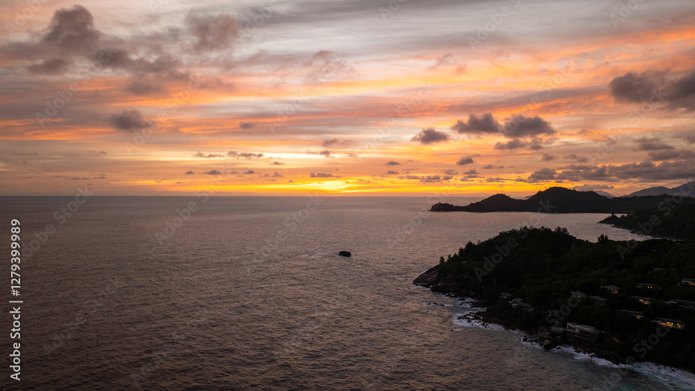 Dark silhouettes of islands stand against a warm sky at twilight, reflecting on the water. Seychelles, Mahe. Dark silhouettes of islands stand against a warm sky at twilight, reflecting on the water. Seychelles, Mahe.