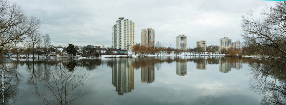 Fototapeta premium A modern residential area by a water body in the city, showcasing new home construction and the demolition of older structures. The urban landscape reflects the transition of winter into spring.