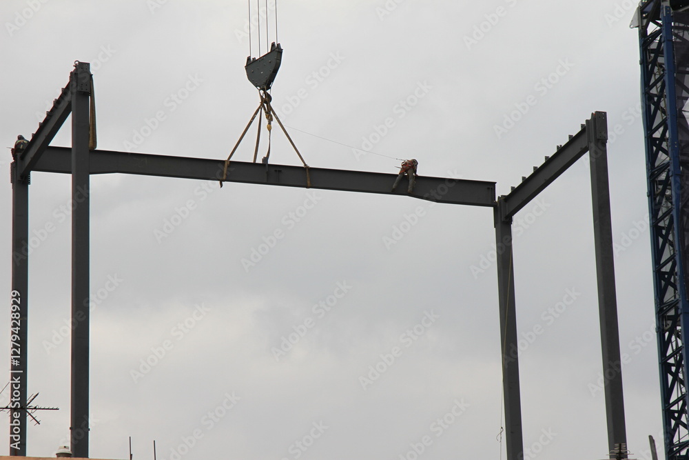 A construction worker on a steel beam in the heights while it is being transported by a construction crane. A man working in the construction. A construction worker on a steel beam in the heights while it is being transported by a construction crane. A man working in the construction.