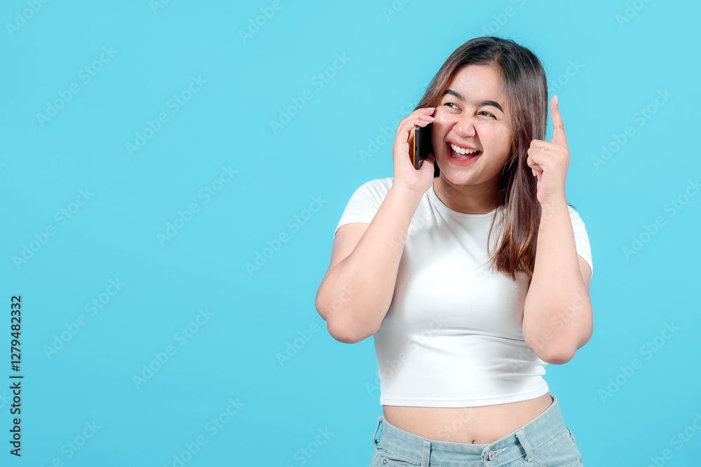 A cheerful young woman talks on her smartphone, showing a happy expression while pointing her finger up, against a bright blue background. A cheerful young woman talks on her smartphone, showing a happy expression while pointing her finger up, against a bright blue background.
