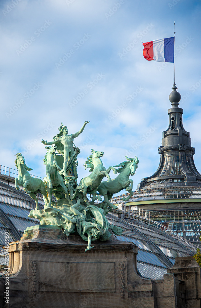 Fototapeta premium A dramatic Quadriga sculpture dominates the foreground, set against a classic Parisian architectural backdrop. The French flag waves proudly in the sky on a sunny, summer day in Paris, France.