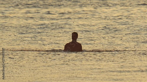 Male surfer sitting on his surfboard in the ocean and splashing water. Tropical water of Indian Ocean. Golden hour light