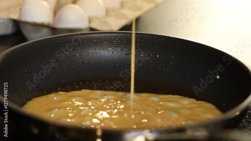 Close up of making scrambled omelet egg in a pan, blurred kitchen table background with white eggs