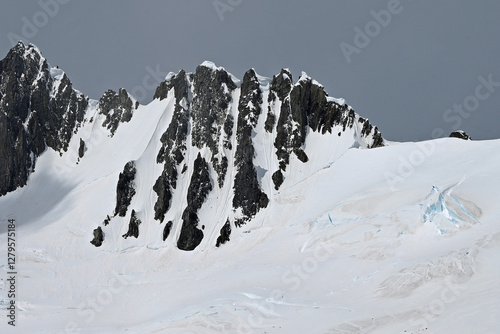 Jabet Peak, Wiencke Island, Antarctica, rises so steeply that snow has a hard time sticking to the basalt rock. Grooves can be seen between the steep rock, evidence of falling snow and ice. photo