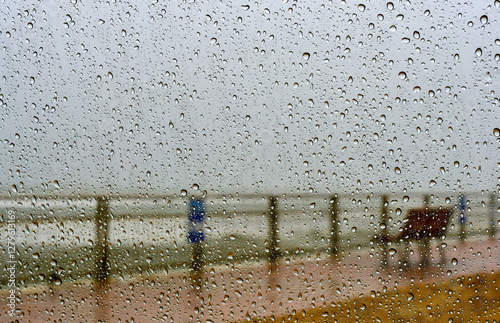 Light rain on the sea coast. Ocean bad weather and empty bench for rest without people.