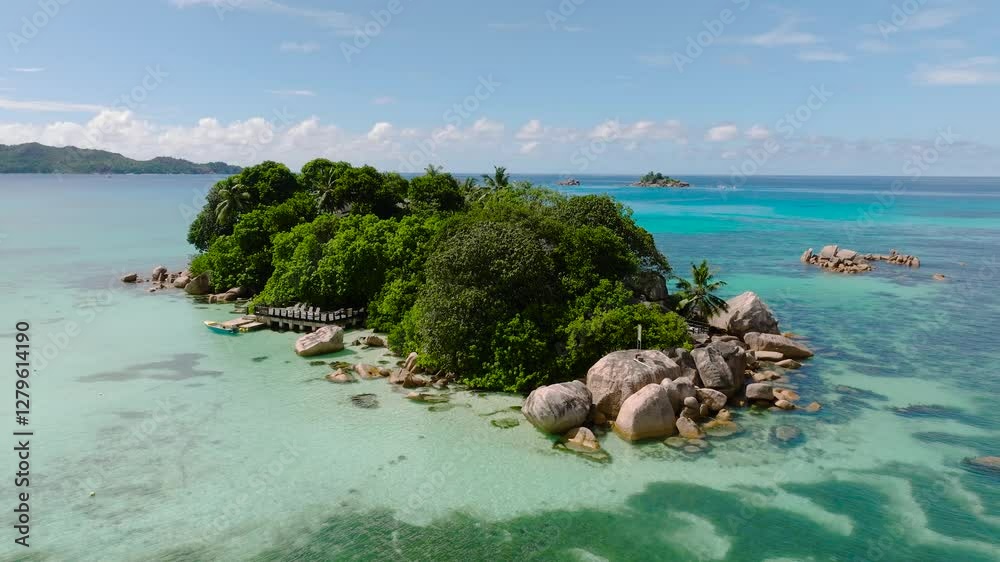 A lush green island rests in tranquil turquoise waters, with rocky shores and tropical beauty. Seychelles.