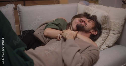 Happy brunette girl hugging with her boyfriend while lying on the sofa in the evening at home