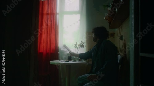 Full medium lowkey shot of disheveled-looking man feeling depressed after receiving past due bills, wandering round kitchen and taking seat in despair