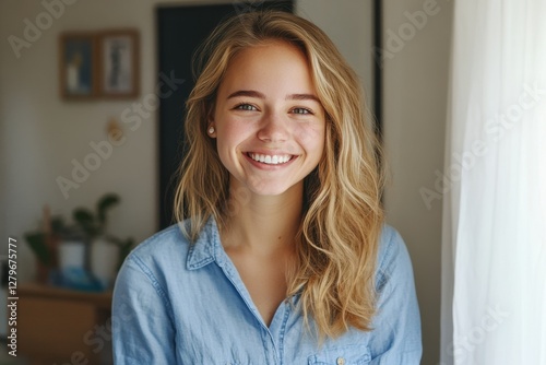 Happy young European woman in blue shirt admiring her healthy skin in the mirror smiling
