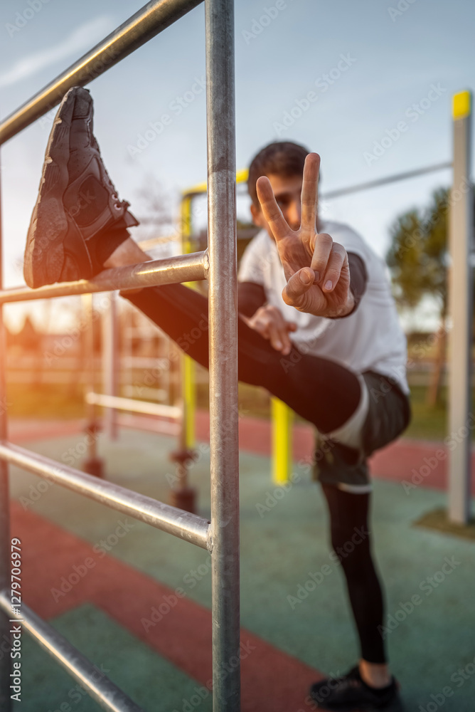 Obraz premium young athletic man exercising at fitness calisthenics workout and stretching legs at street gym during sunset, body improvement and strength training concept