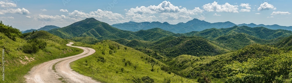 Fototapeta premium Scenic Winding Road Through Lush Green Mountains Under Blue Sky with White Clouds