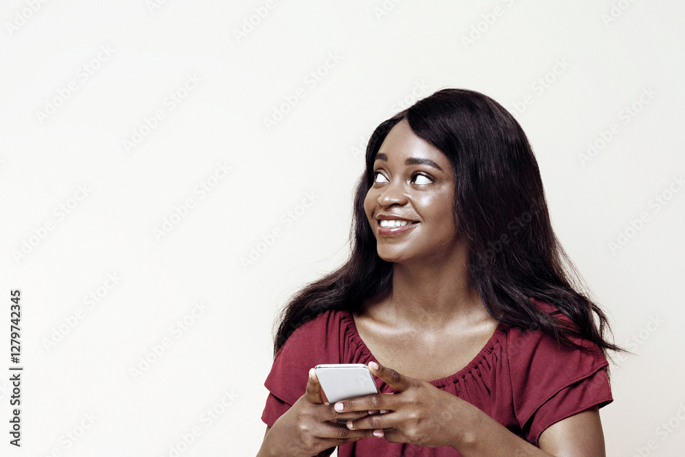 Pretty long-haired young black woman with newest cellphone sitting on floor, looking at copy space over beige studio background, using nice dating, entertaining mobile app on smartphone, panorama Pretty long-haired young black woman with newest cellphone sitting on floor, looking at copy space over beige studio background, using nice dating, entertaining mobile app on smartphone, panorama