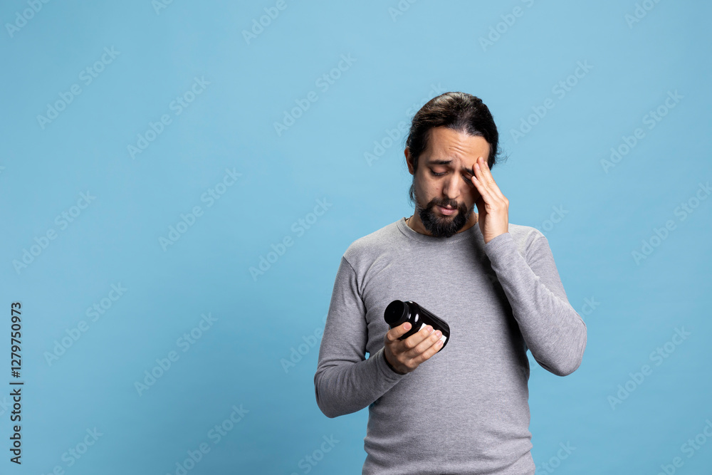 Sick person taking pills from the jar against blue background, having a medication treatment with antibiotics as a remedy for wellness. Young man takes painkillers to relieve the pain. Sick person taking pills from the jar against blue background, having a medication treatment with antibiotics as a remedy for wellness. Young man takes painkillers to relieve the pain.