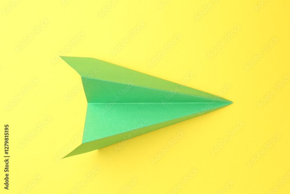 One handmade green paper plane on yellow background, top view One handmade green paper plane on yellow background, top view