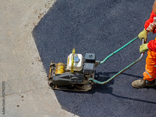 Male industrial worker using plate compactor tool outside on street asphalt