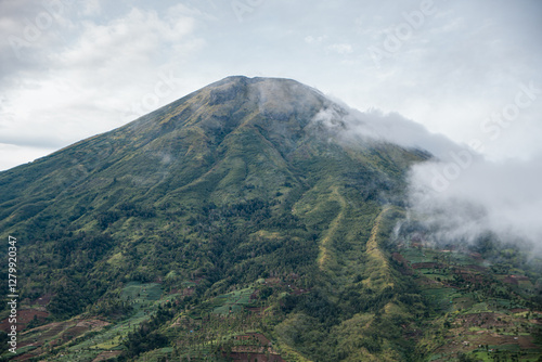 Landscape Mount Sindoro from a close distance with clouds around the peak on a sunny morning. The beautiful and green view of Mount Sindoro from the top of the hill at an altitude of 1800 mdpl photo