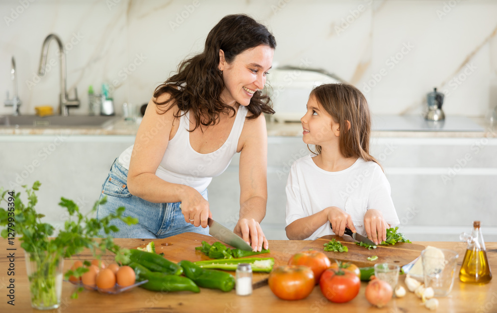 Happy mother and her little daughter are cutting fresh vegetables for salad in the kitchen Happy mother and her little daughter are cutting fresh vegetables for salad in the kitchen