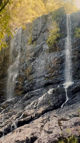 A breathtaking waterfall tumbles down rocky cliffs, surrounded by lush green vegetation, creating a natures serene and magical vertical video background.