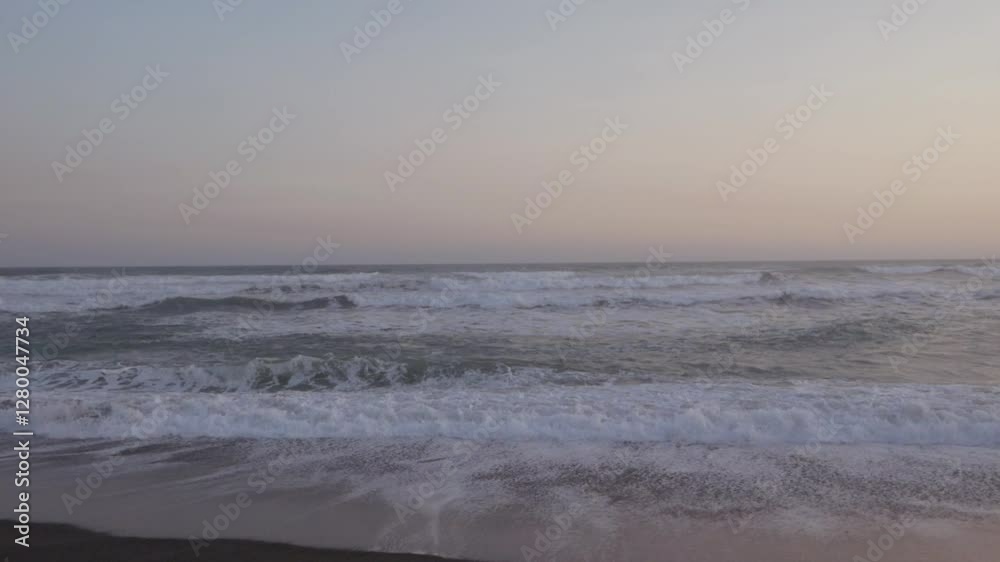 Handheld view of gentle ocean waves crashing on a black sand beach during twilight at a coastal location in Indonesia Handheld view of gentle ocean waves crashing on a black sand beach during twilight at a coastal location in Indonesia