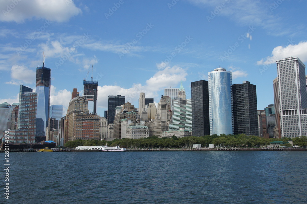 Obraz premium New York Harbor panorama: Lady Liberty in the foreground, with Manhattan's southern tip and towering skyscrapers stretching across the water. An enduring symbol greeting a bustling city.