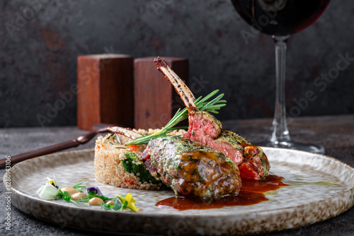  Grilled racks of lamb with demiglas sauce and vegetables and quinoa on a grey plate. Main course of lamb ribs, close up
