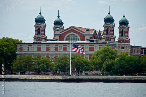 Obraz na plátně A large red brick building with two towers stands in New York Harbor, a flag proudly waving in front