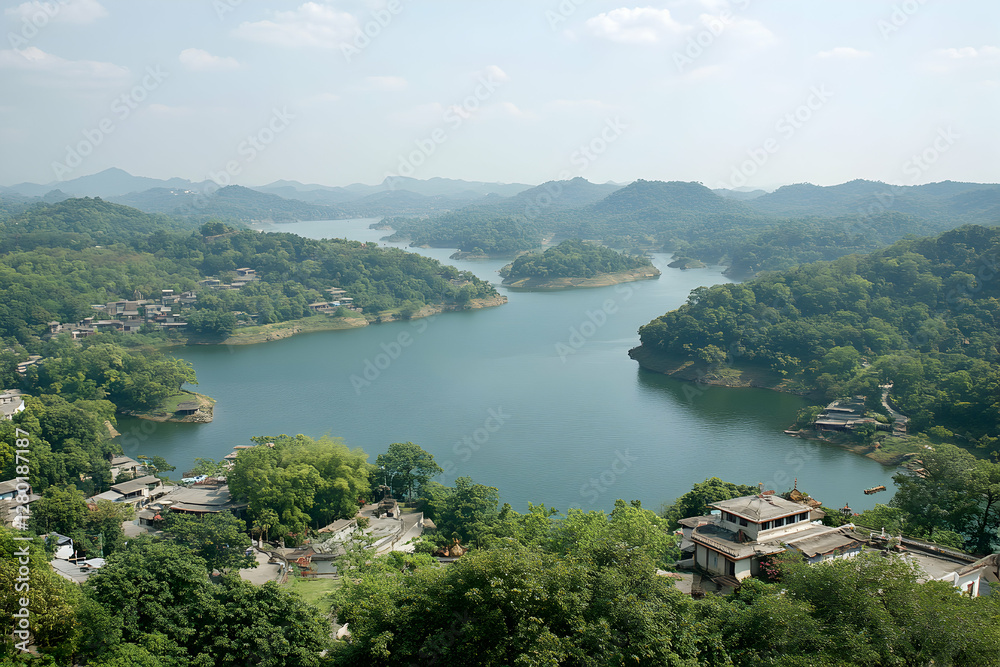 Fototapeta premium Serene aerial view of a picturesque lake nestled within lush green mountains, showcasing a tranquil village and traditional architecture.