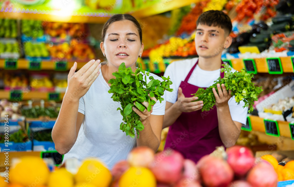 Friendly guy seller helps a girl buyer who came to the store for shopping, choose a fresh greenery Friendly guy seller helps a girl buyer who came to the store for shopping, choose a fresh greenery