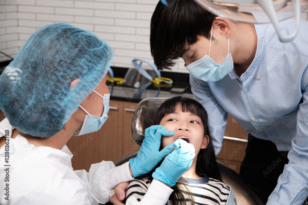 Obraz premium Asian female pediatric dentist examines a girl's teeth in dental clinic and takes care and encourages of father, mouth oral hygiene, and professional orthodontic healthcare work in a kid hospital.