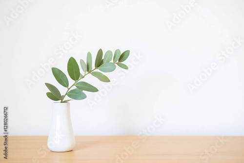small white vase with single eucalyptus branch on wooden surface