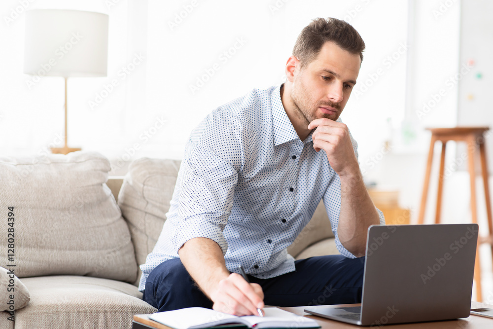 Self Education At Home. Concentrated man holding pen and looking at laptop sitting in living room, free space