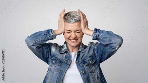 Headache Concept. Sick mature woman touching her temples, suffering from migraine or stress, emotionally reacting to acute pain, light background
