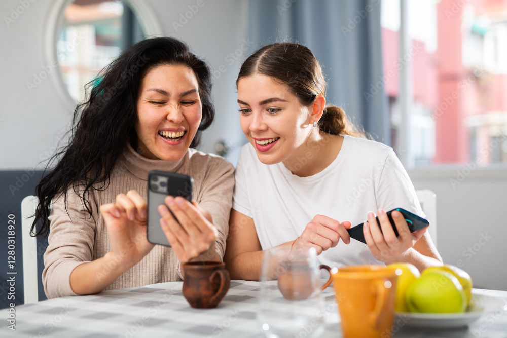 Positive adult girlfriends typing text on phone and talking on the speakerphone Positive adult girlfriends typing text on phone and talking on the speakerphone