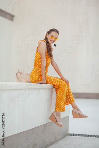 a beautiful girl in a bright clothes walks around the city in the summer. Young womn smiling against the biege wall and sun kight photo